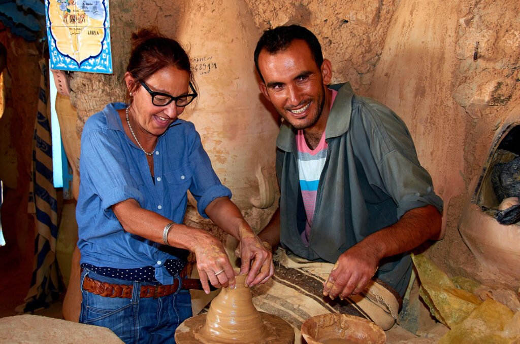 Verena, Organisatorin von Saharawalk, macht aus Ton eine Blumenvase im Tonatelier von Guellela, Djerba. Der Inhaber leitet sie an.