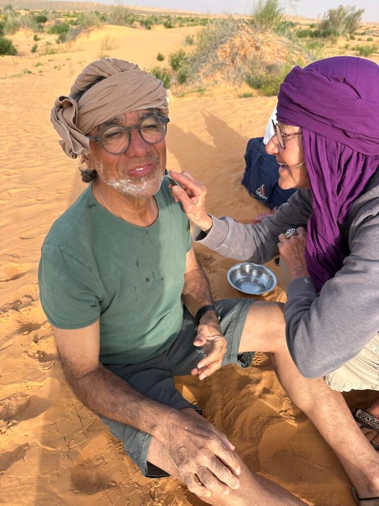 Zwei Teilnehmer einer Saharawalk-Reise sitzen entspannt auf einer hohen Sanddüne in der tunesischen Wüste.